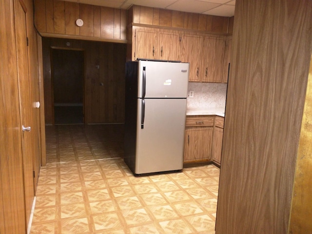 kitchen featuring wooden walls, light floors, brown cabinetry, and freestanding refrigerator