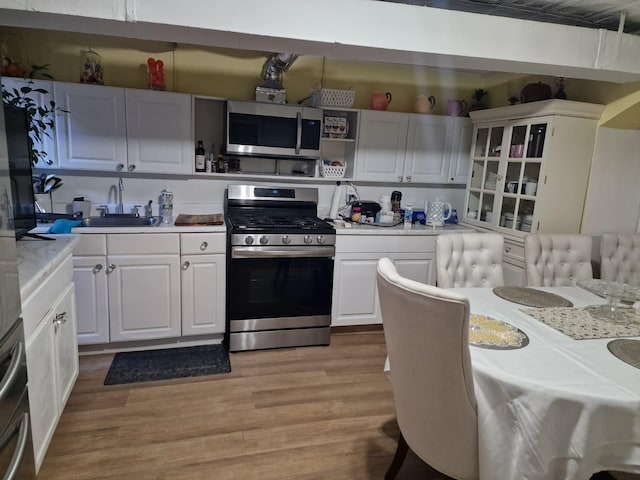 kitchen featuring light countertops, light wood-style flooring, white cabinets, stainless steel appliances, and a sink