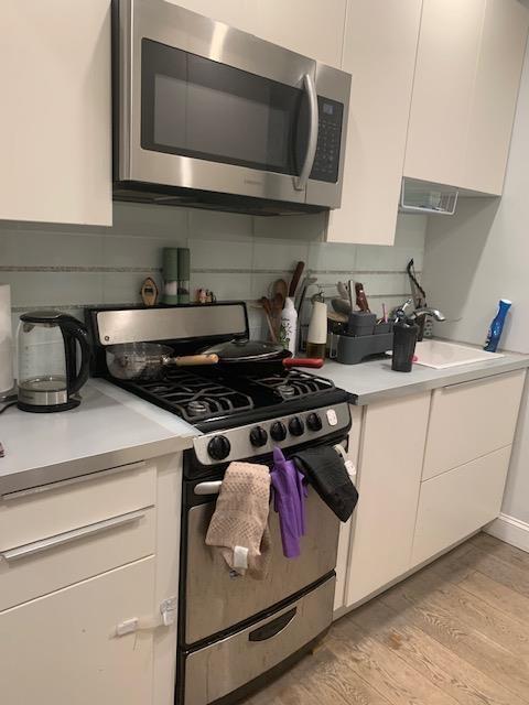 kitchen featuring white cabinets, stainless steel appliances, light countertops, and light wood-style floors