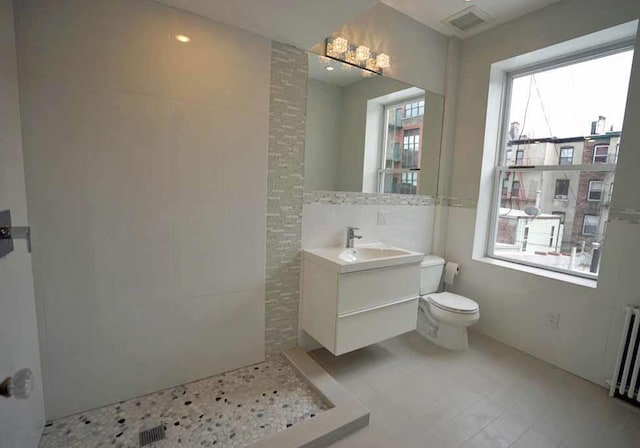 full bath featuring visible vents, radiator, toilet, tiled shower, and vanity