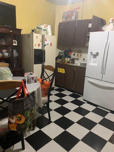 kitchen with backsplash, light floors, white refrigerator with ice dispenser, and dark brown cabinetry