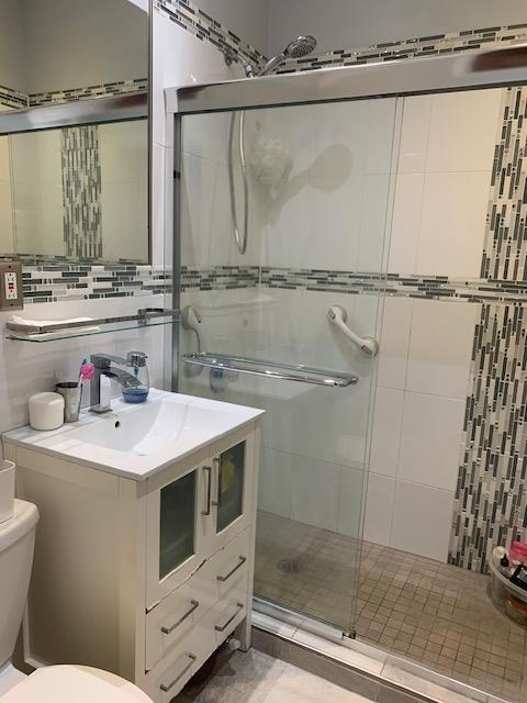 bathroom with toilet, vanity, decorative backsplash, a stall shower, and tile walls