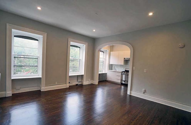 unfurnished living room featuring arched walkways, recessed lighting, dark wood-type flooring, and baseboards