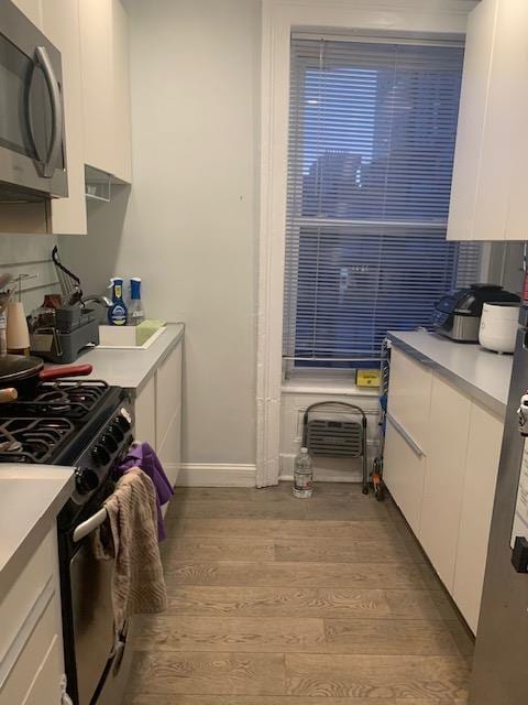 kitchen featuring stainless steel microwave, light wood-style floors, black range with gas cooktop, and white cabinetry