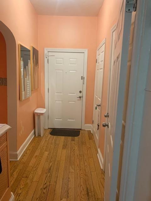 entryway featuring arched walkways, light wood-style flooring, and baseboards