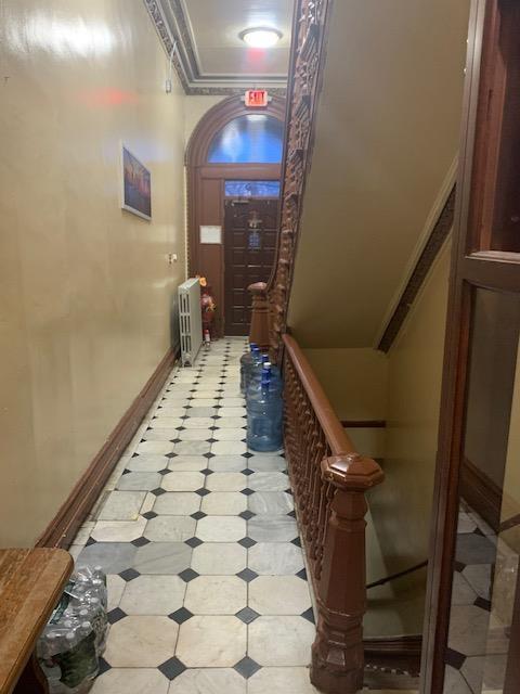 corridor with light floors, radiator, crown molding, and baseboards