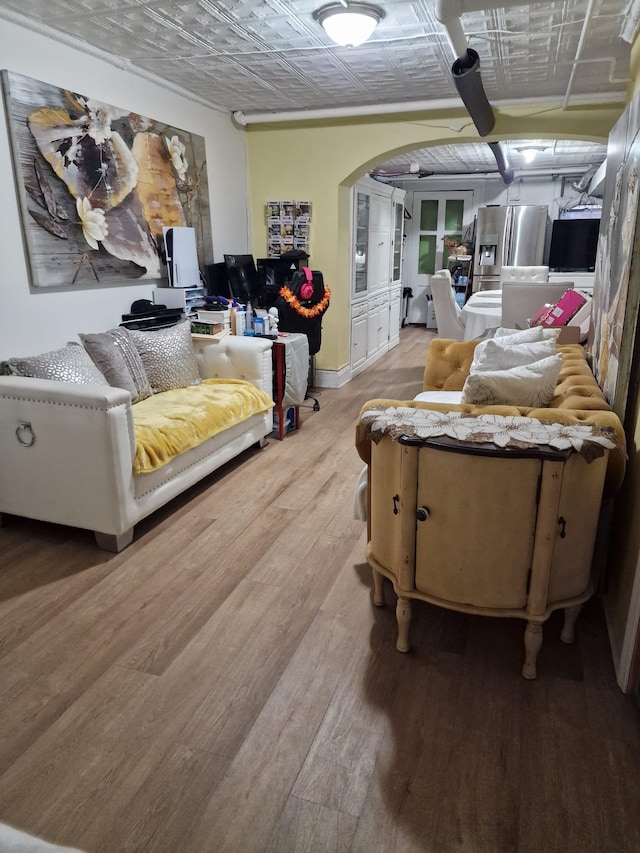 living room featuring baseboards, an ornate ceiling, arched walkways, and light wood finished floors