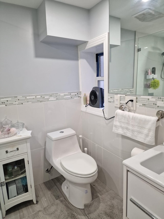 bathroom featuring walk in shower, toilet, vanity, wood finished floors, and tile walls