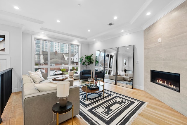 living room with a fireplace, light wood-type flooring, a raised ceiling, and crown molding