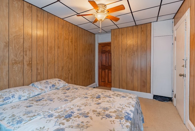 bedroom featuring ceiling fan, wooden walls, and a drop ceiling