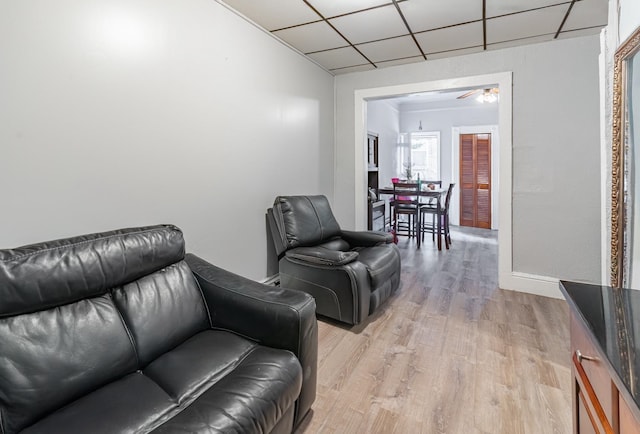 living room featuring ceiling fan, a drop ceiling, and light hardwood / wood-style floors