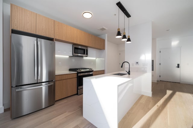 kitchen with pendant lighting, stainless steel appliances, sink, kitchen peninsula, and light hardwood / wood-style flooring