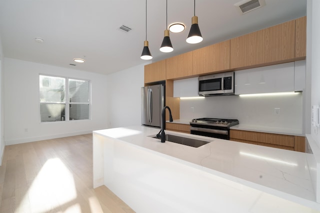 kitchen featuring stainless steel appliances, hanging light fixtures, light hardwood / wood-style flooring, light stone counters, and sink