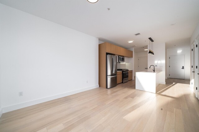 kitchen with appliances with stainless steel finishes, sink, hanging light fixtures, a kitchen island with sink, and light wood-type flooring