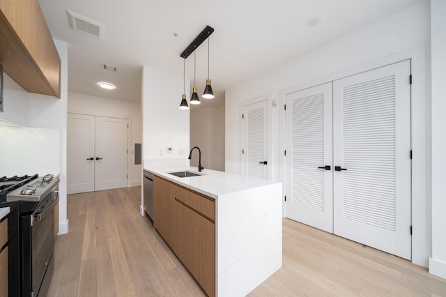 kitchen with decorative light fixtures, dishwasher, range with gas stovetop, light stone counters, and sink