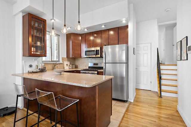 kitchen featuring tasteful backsplash, glass insert cabinets, light stone countertops, appliances with stainless steel finishes, and a peninsula