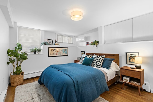 bedroom featuring a wall unit AC, wood finished floors, and baseboard heating