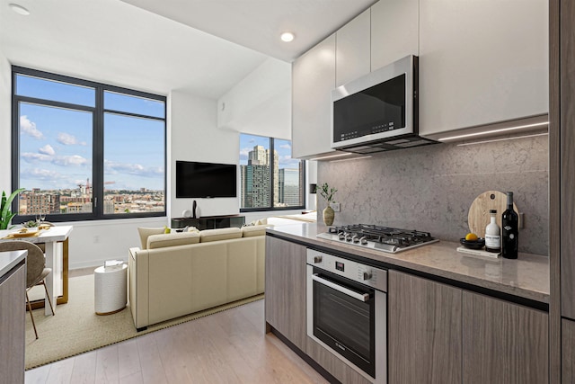 kitchen with decorative backsplash, stainless steel appliances, light hardwood / wood-style floors, and white cabinets