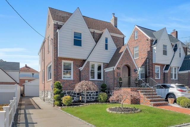 tudor home with fence, an outdoor structure, a front lawn, a garage, and brick siding