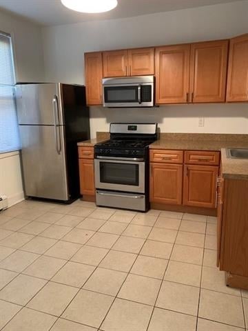 798 Grand St, Jersey City, NJ 07304 - kitchen with stainless steel appliances, brown cabinetry, and light tile patterned floors