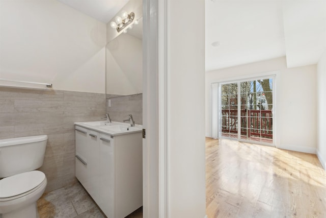 half bath with toilet, vanity, wainscoting, wood finished floors, and tile walls