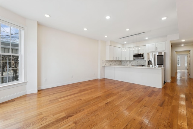 kitchen featuring tasteful backsplash, light wood finished floors, light countertops, stainless steel appliances, and white cabinetry