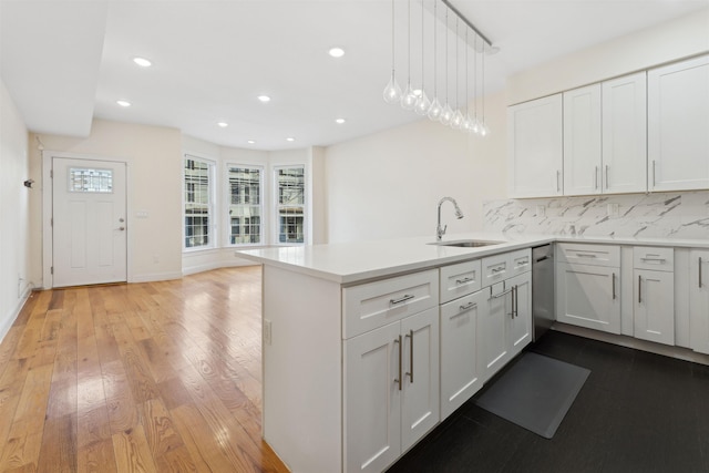 kitchen with light wood-type flooring, a sink, backsplash, white cabinetry, and a peninsula