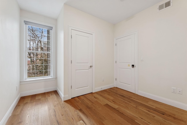 unfurnished bedroom with visible vents, multiple windows, baseboards, and light wood-style flooring