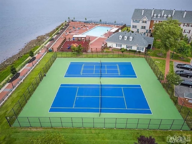 view of tennis court featuring a water view and fence