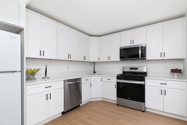 kitchen with light wood-type flooring, appliances with stainless steel finishes, white cabinets, and light countertops