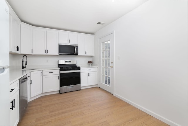 kitchen featuring light countertops, appliances with stainless steel finishes, light wood-style floors, white cabinets, and a sink