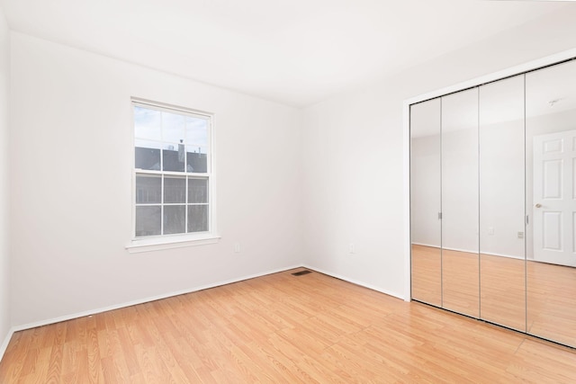 unfurnished bedroom featuring light wood-style floors, visible vents, baseboards, and a closet