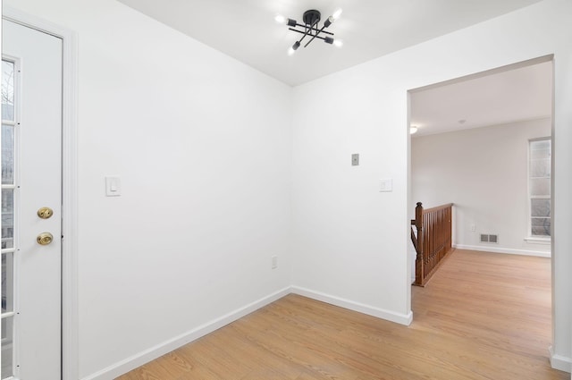 empty room with a notable chandelier, light wood-style flooring, visible vents, and baseboards