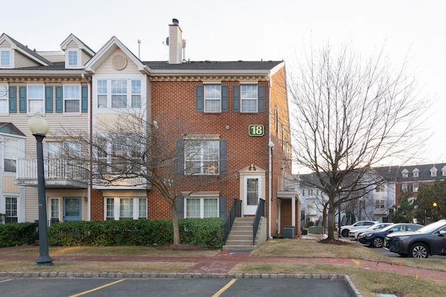 multi unit property featuring uncovered parking, a chimney, cooling unit, and brick siding