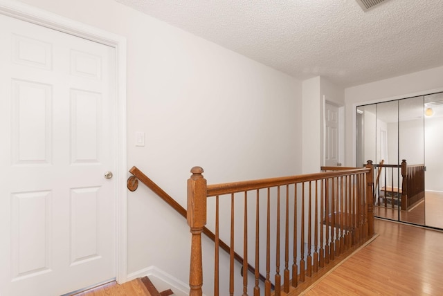 hall featuring a textured ceiling, wood finished floors, an upstairs landing, and baseboards