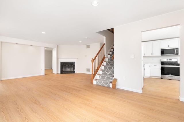 unfurnished living room featuring light wood finished floors, visible vents, stairway, a glass covered fireplace, and baseboards