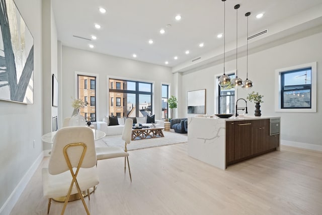 kitchen featuring sink, hanging light fixtures, dark brown cabinets, a center island with sink, and light wood-type flooring