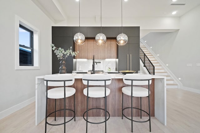 kitchen featuring a kitchen breakfast bar, a kitchen island with sink, light hardwood / wood-style flooring, and hanging light fixtures