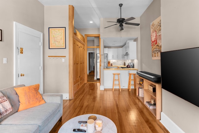 living area with baseboards, a ceiling fan, and light wood-style flooring