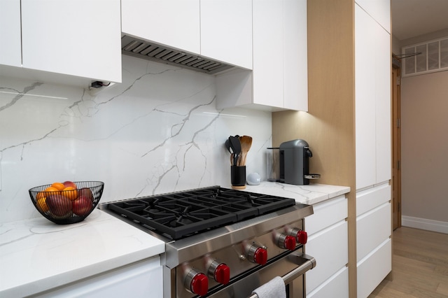 kitchen featuring high end stainless steel range oven, visible vents, tasteful backsplash, light stone counters, and white cabinetry