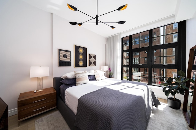 bedroom featuring an inviting chandelier, a high ceiling, floor to ceiling windows, and wood finished floors