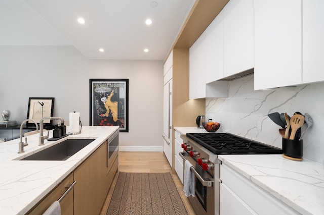 kitchen with decorative backsplash, recessed lighting, light wood-type flooring, a sink, and high end range