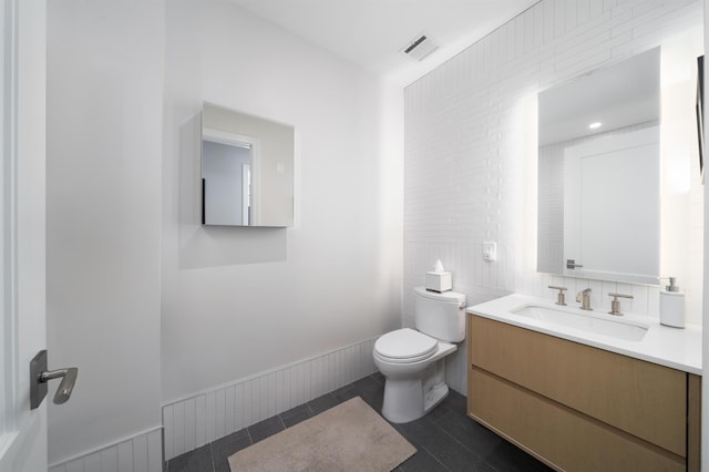 half bathroom featuring vanity, toilet, tile patterned floors, tile walls, and visible vents