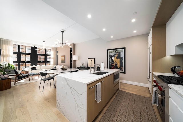 kitchen featuring a kitchen island with sink, modern cabinets, a sink, light wood finished floors, and stainless steel appliances