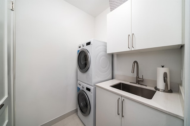 washroom featuring cabinet space, stacked washing maching and dryer, light tile patterned floors, baseboards, and a sink