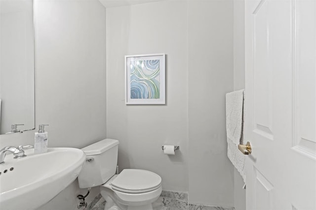 half bath with marble finish floor, a sink, toilet, and baseboards