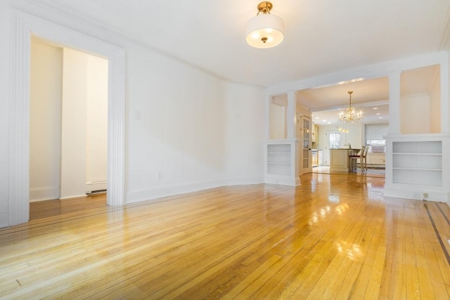 unfurnished living room with built in shelves, light hardwood / wood-style flooring, ornamental molding, and a notable chandelier