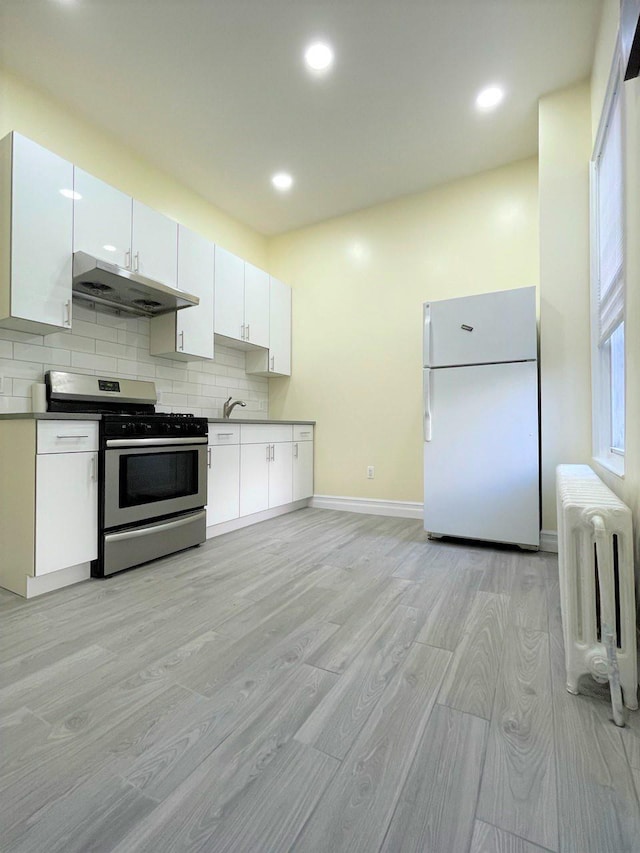 kitchen with light wood-type flooring, radiator, white refrigerator, stainless steel range oven, and white cabinetry