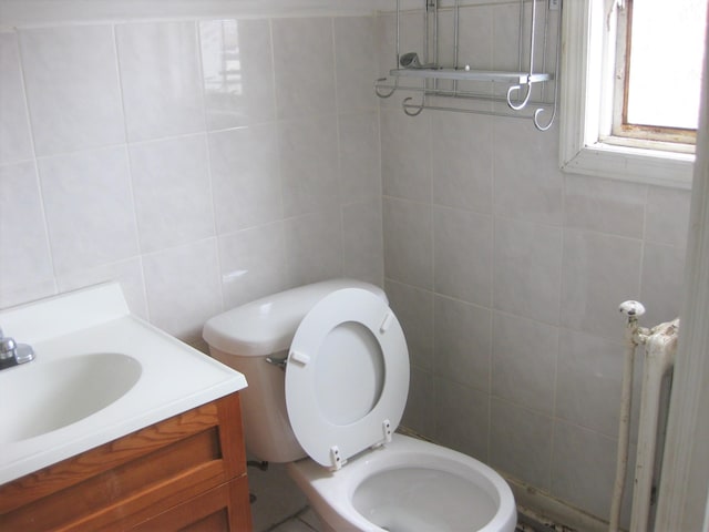 bathroom with vanity, toilet, radiator heating unit, and tile walls