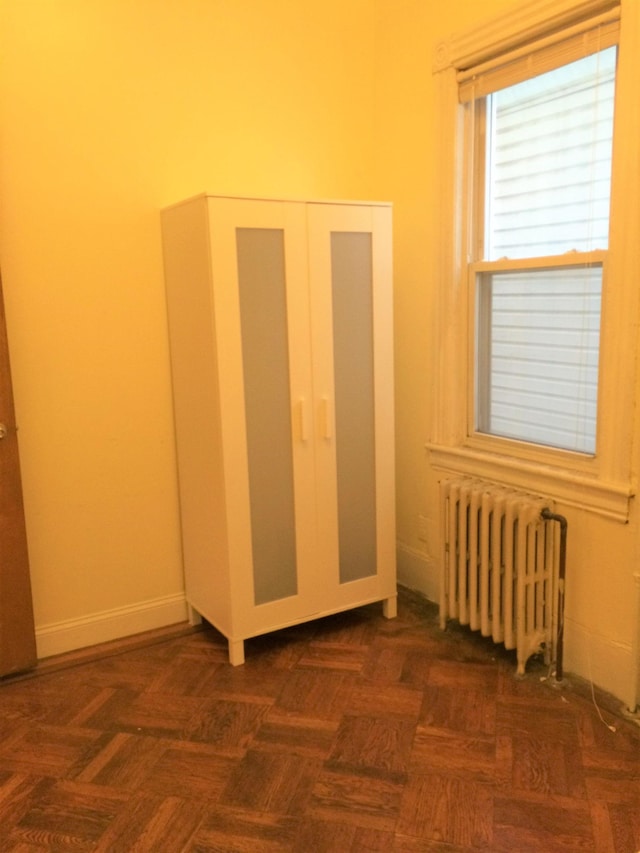 unfurnished bedroom with dark parquet flooring, a closet, and radiator heating unit